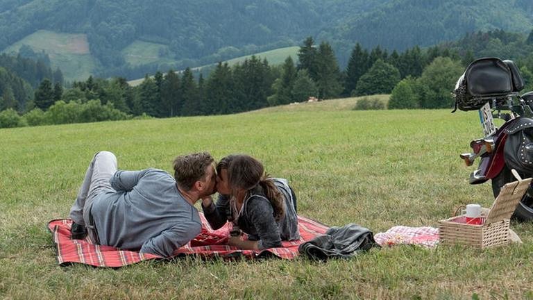 Andreas und Eva liegen auf ihrer Picknickdecke und küssen sich