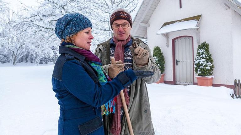 Bea und Karl stehen im Schnee vor der Hofkapelle und betrachten eine Patronenhülse