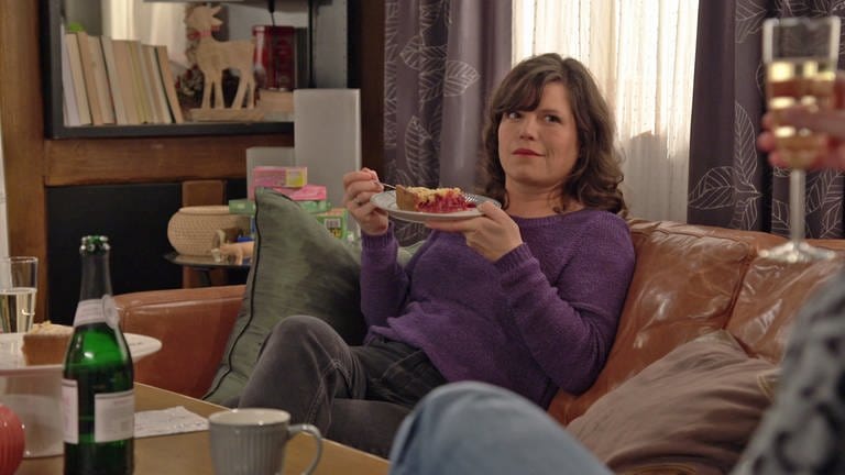 Eva sitzt auf dem Sofa und hält vor sich einen Teller mit Träubleskuchen