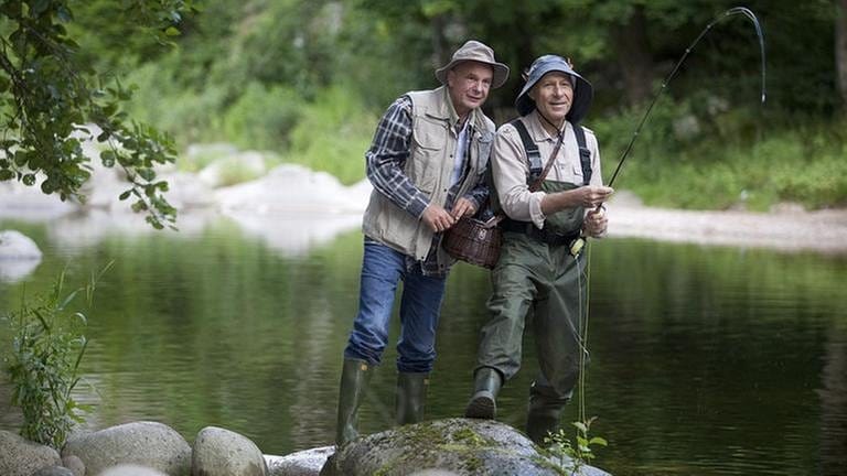 Franz und Heinz stehen auf einem großen Flusskiesel und angeln