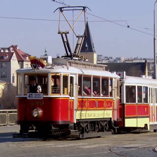 Historischer roter Zug in Prager Altstadt mit Lokführer und mehreren Menschen im Abteil