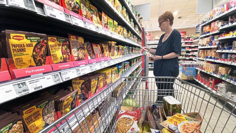 Frau mit Einkaufswagen im Supermarkt vor einem Regal mit Produkten von Maggi: Schnell und günstig kochen mit Fertigprodukten ist nicht unbedingt auch gesund
